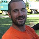 Un homme avec une barbe porte une chemise orange et sourit.