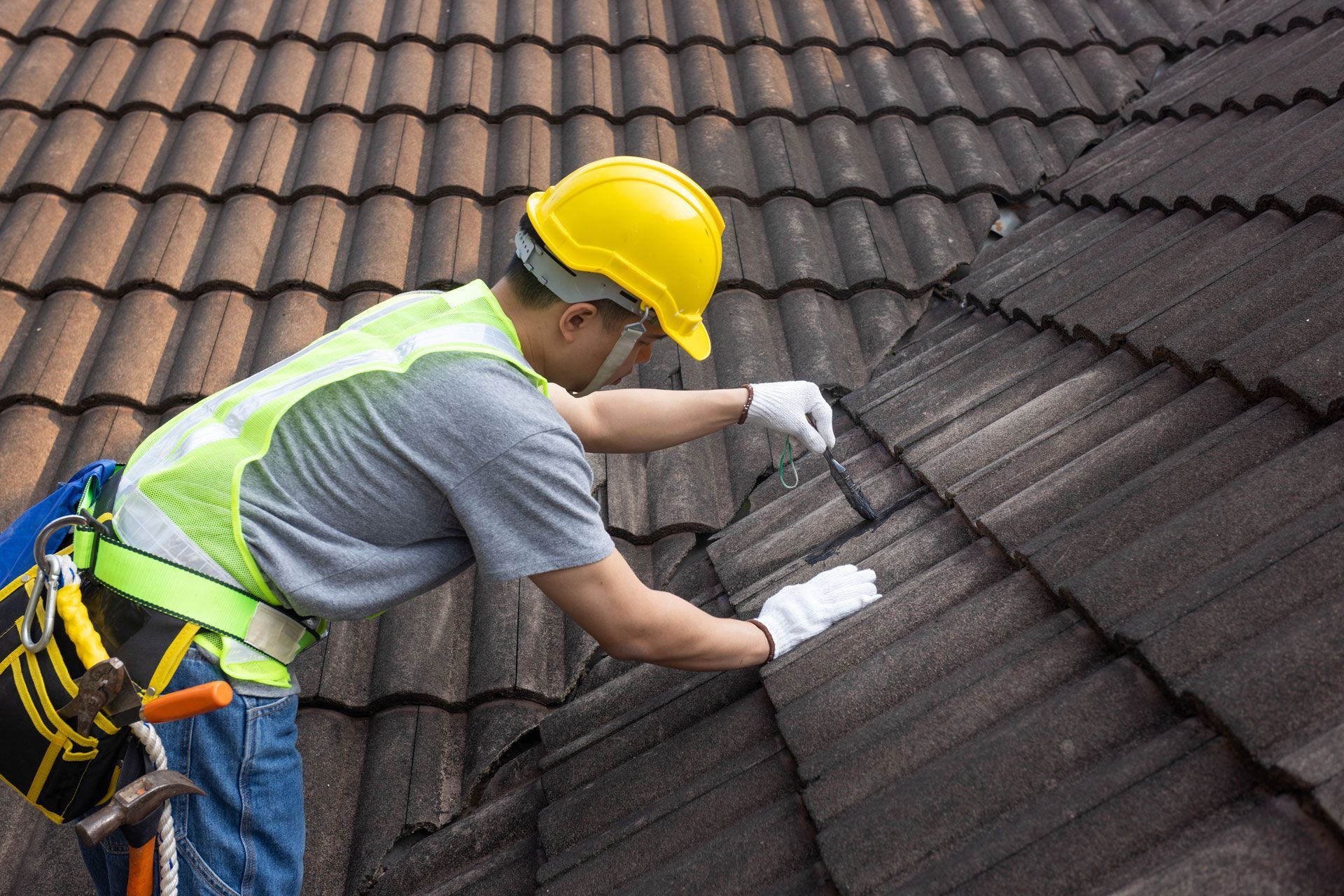 Roofer in yellow helmet and safety vest on a tiled roof.