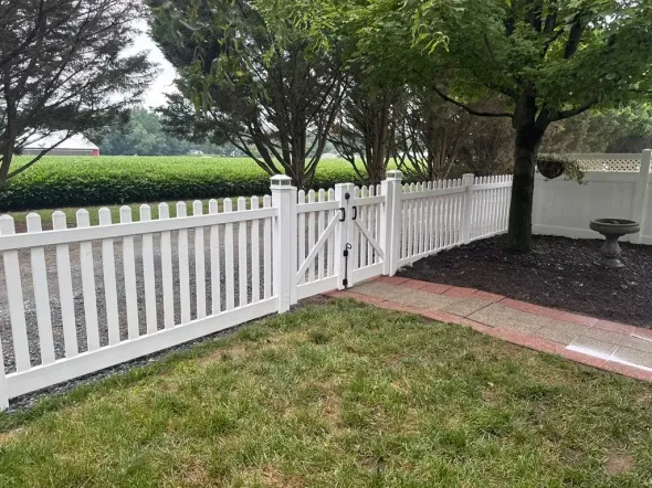 White picket fence with gate in front yard, with trees and green lawn.