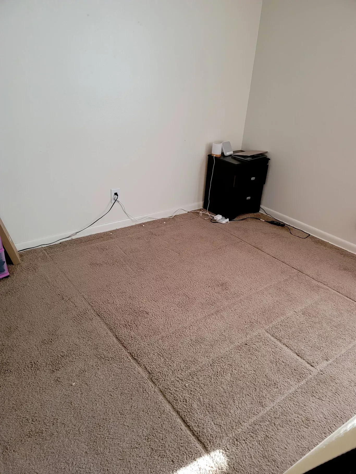 Empty bedroom with beige carpet, a black nightstand, and white walls.