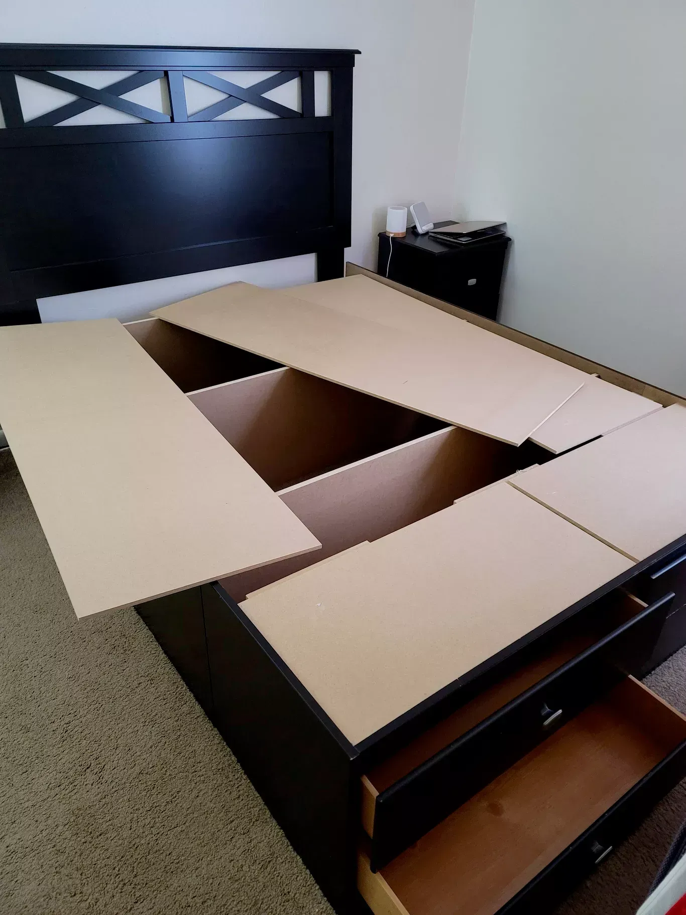 Black bed frame with drawers and hinged sections revealing storage compartments.