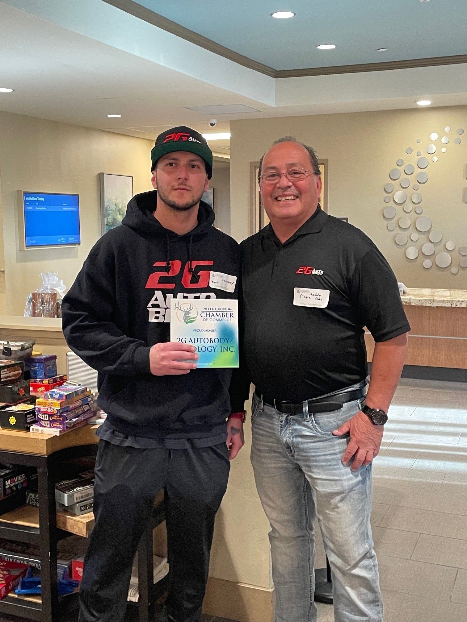 Two men stand near a snack display in a hotel lobby. One holds a booklet. Both smile.