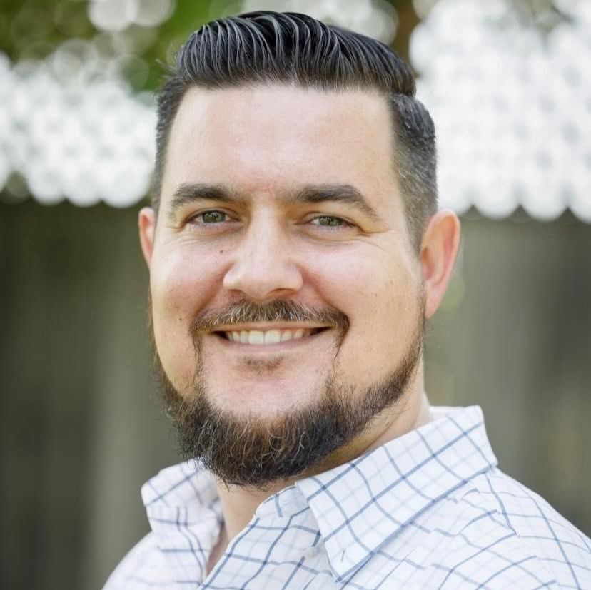 A man with a beard is smiling and wearing a plaid shirt.