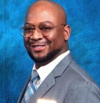 A man in a suit and tie is smiling in front of a blue background