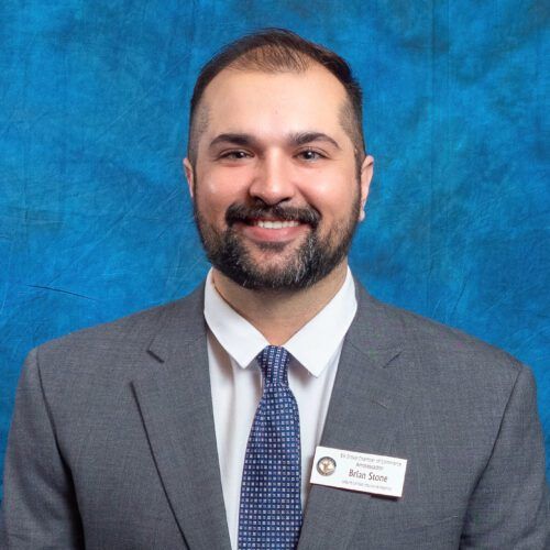 A man in a suit and tie is smiling in front of a blue background.