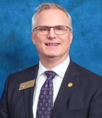 A man in a suit and tie is smiling in front of a blue background