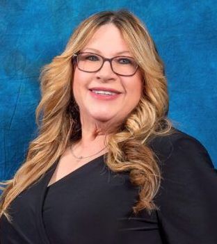 A woman wearing glasses and a black dress is standing in front of a blue background.