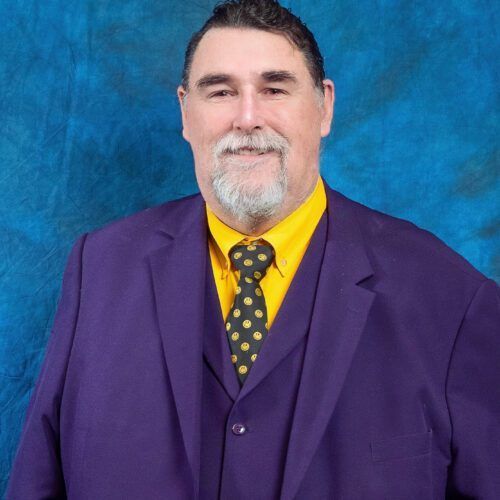A man with a beard wearing a purple suit and tie