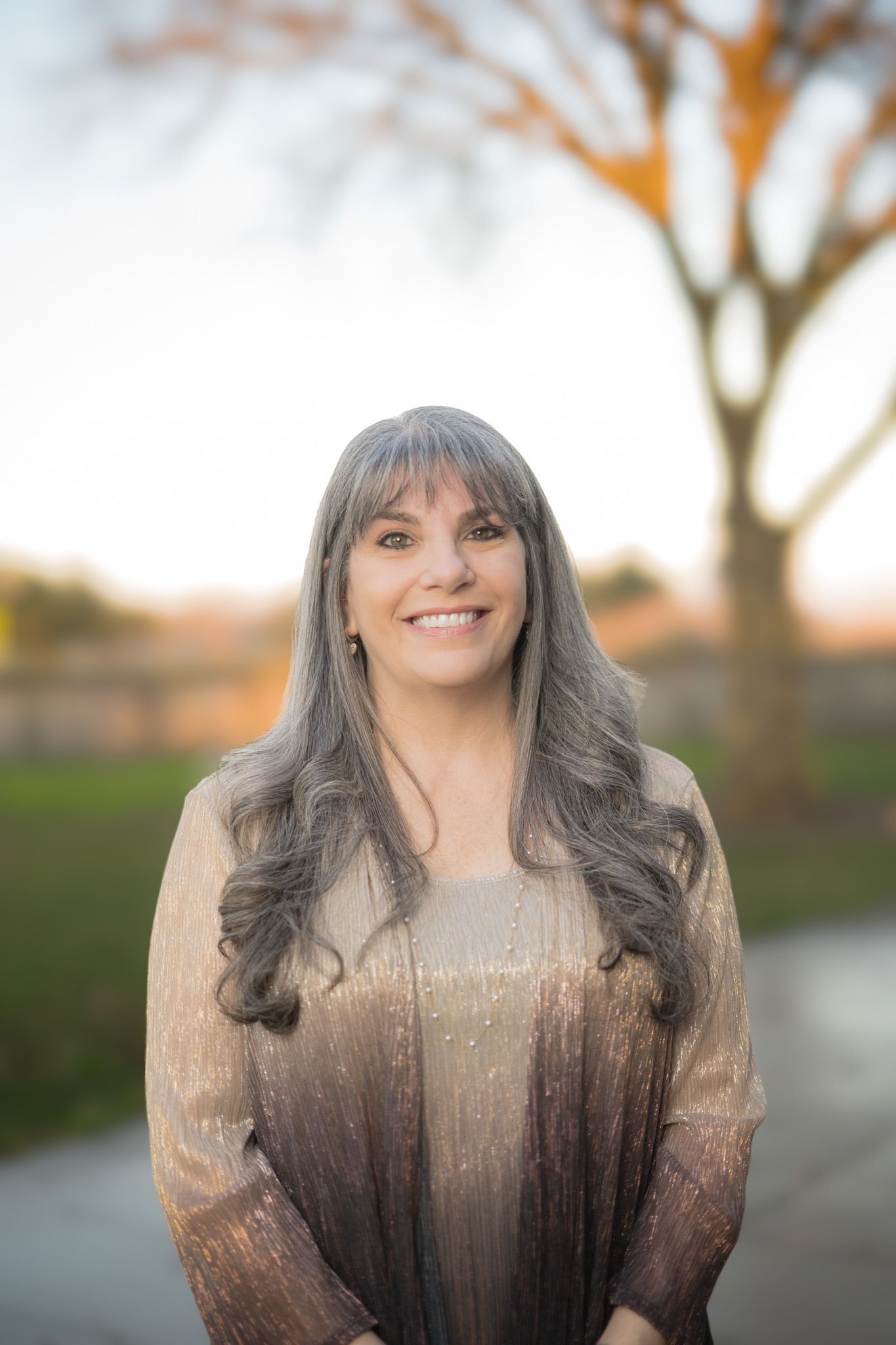A woman with long red hair is wearing a tan jacket and smiling.