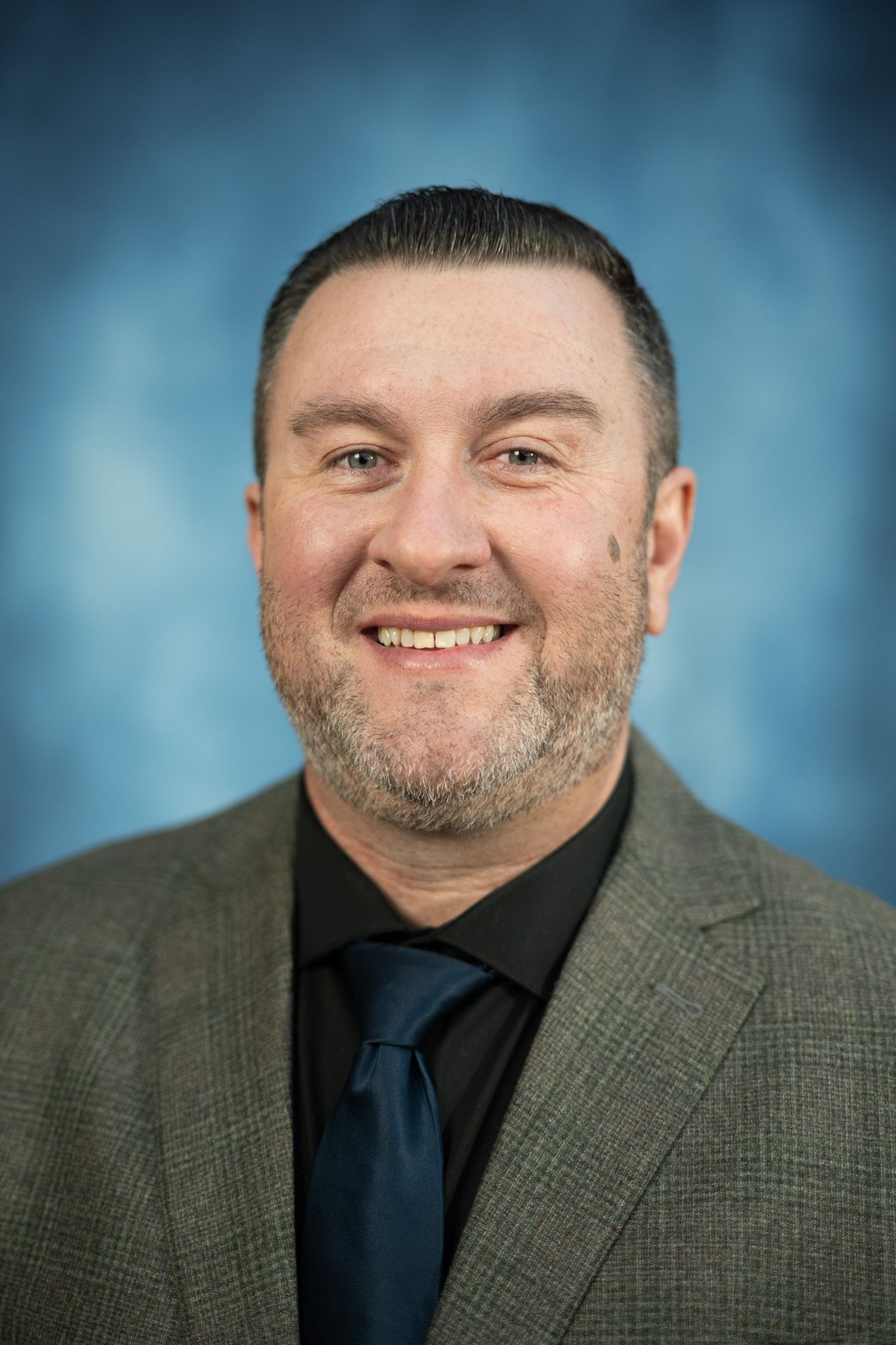 A man in a suit and tie is smiling in front of a blue background.
