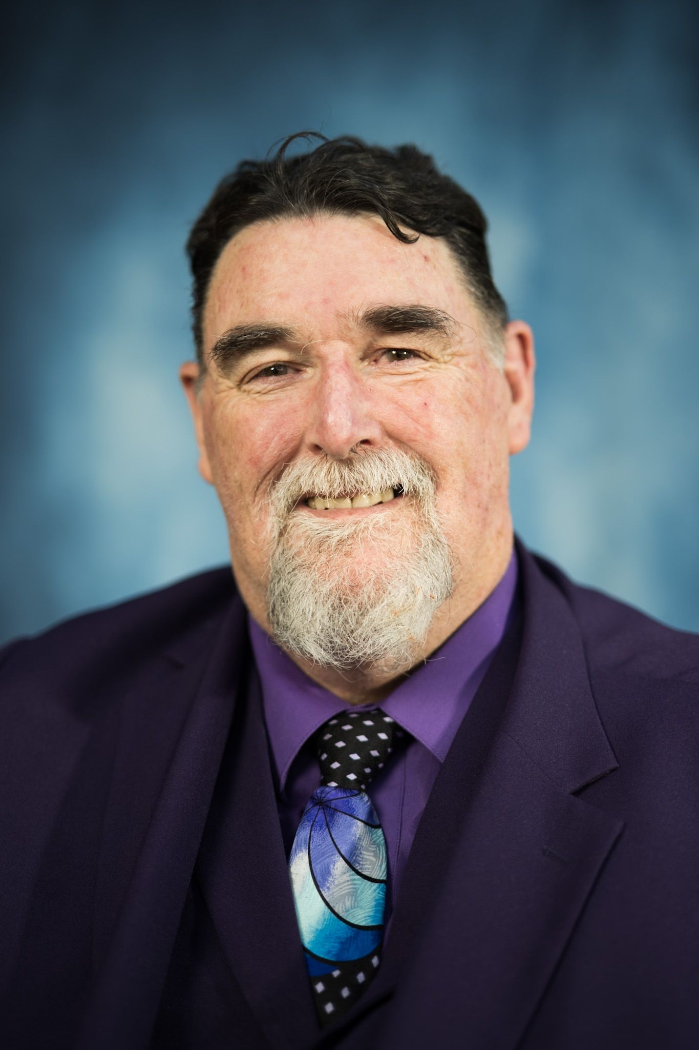 A man with a beard wearing a purple suit and tie