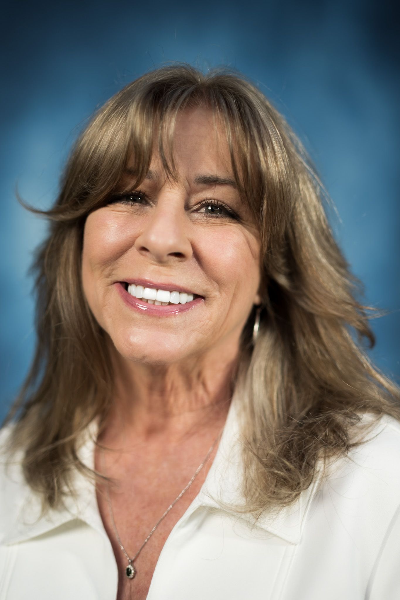 A woman wearing a black polka dot shirt and a necklace is smiling for the camera.