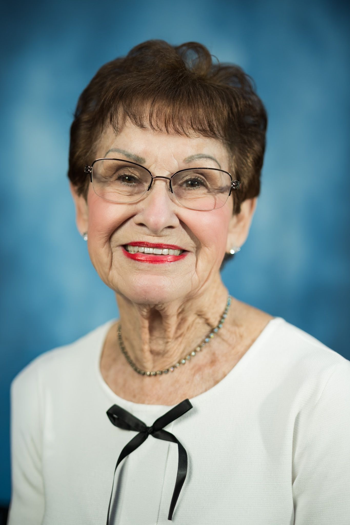 A woman wearing glasses and a necklace is smiling in front of a blue background.