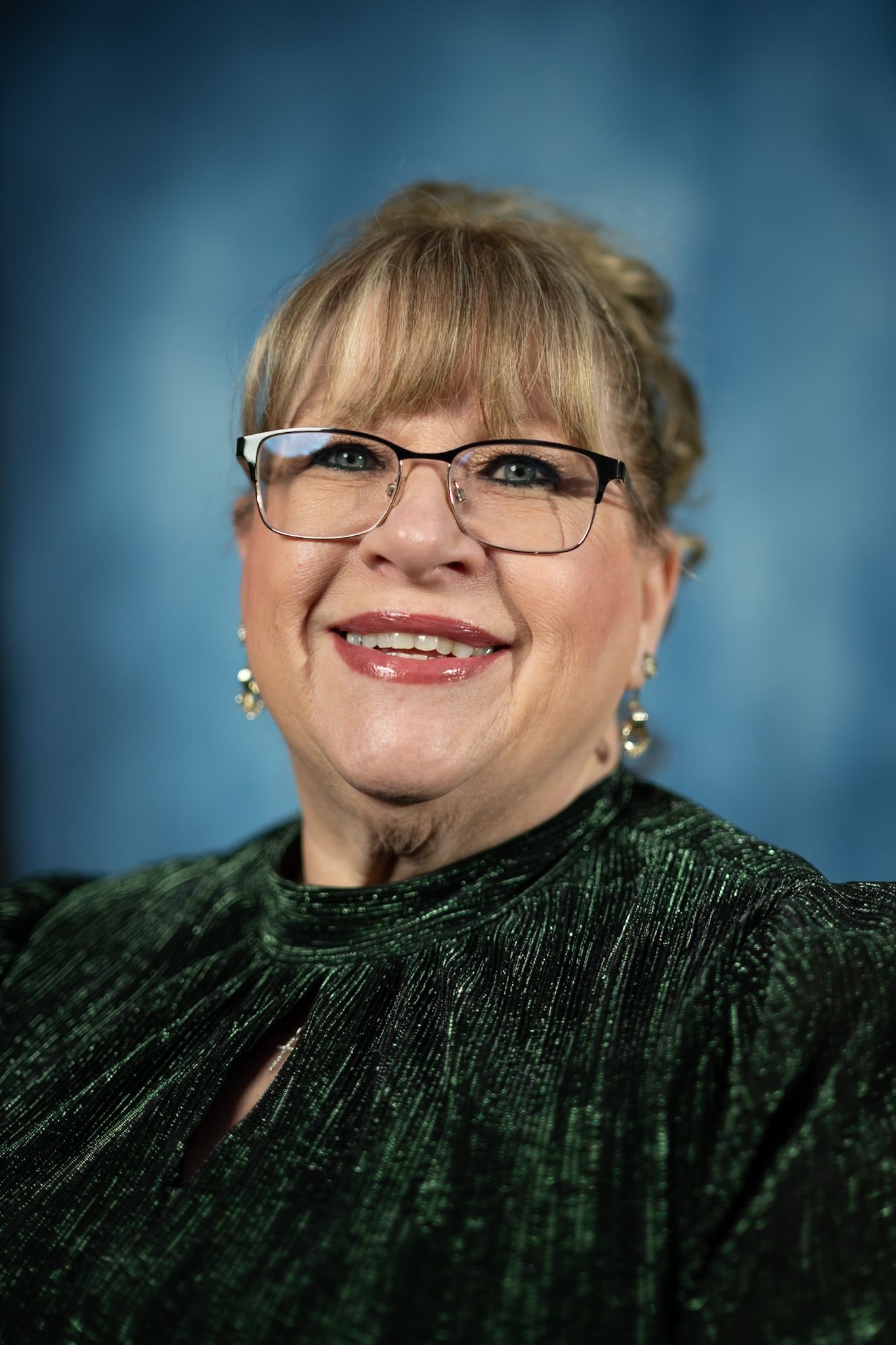 A woman wearing glasses and a black dress is standing in front of a blue background.