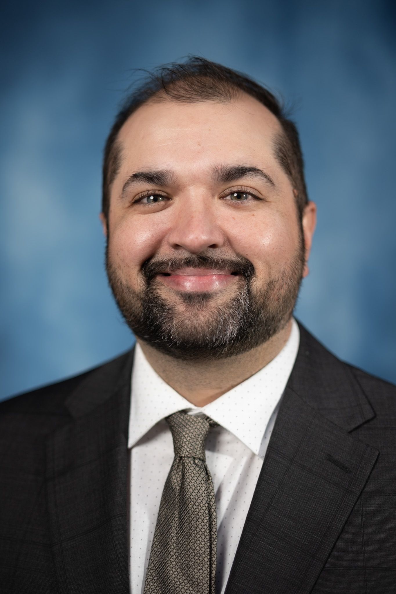 A man in a suit and tie is smiling in front of a blue background.