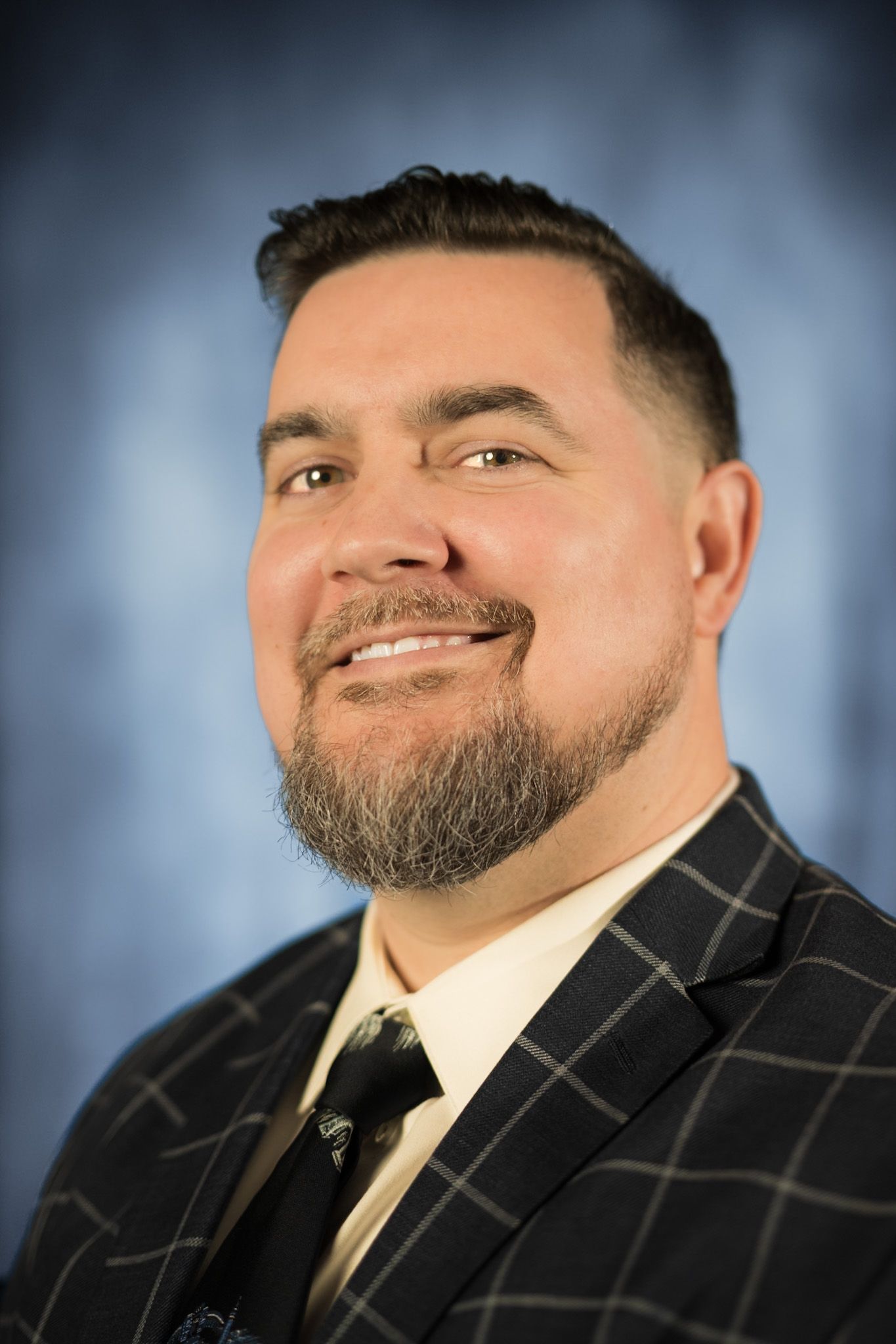 A man with a beard is smiling and wearing a plaid shirt.