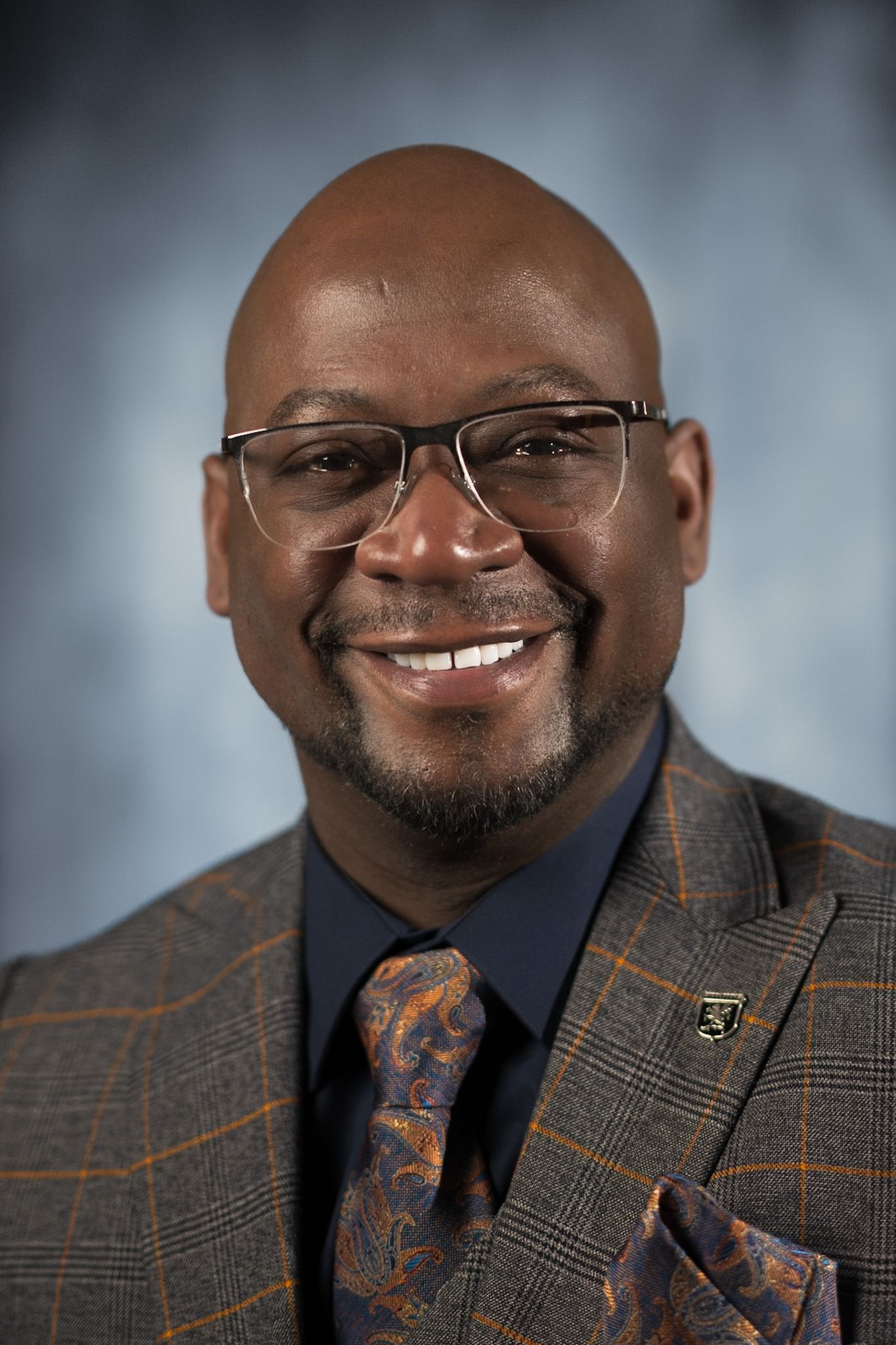 A man in a suit and tie is smiling in front of a blue background