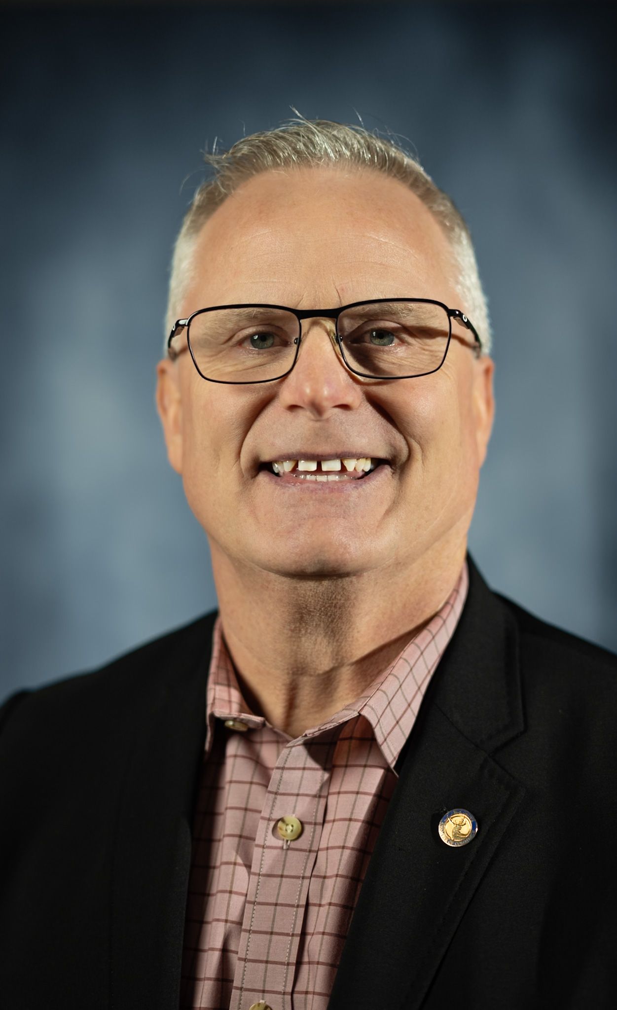 A man in a suit and tie is smiling in front of a blue background