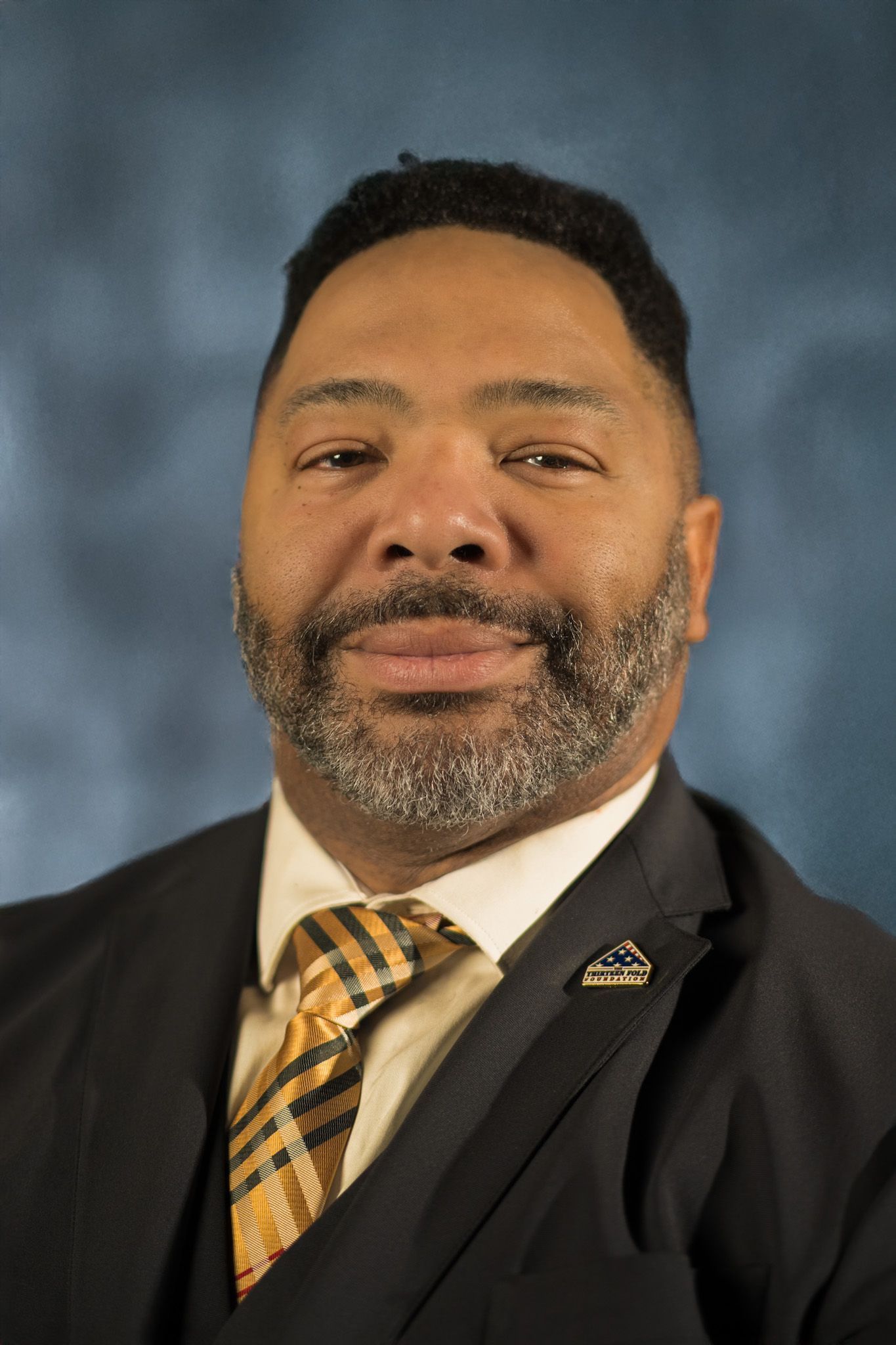 Man in suit and tie, smiling, against a blurred blue background.