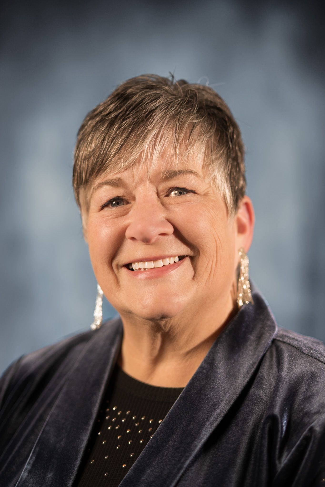 A woman wearing a black shirt and a gray jacket is smiling for the camera.