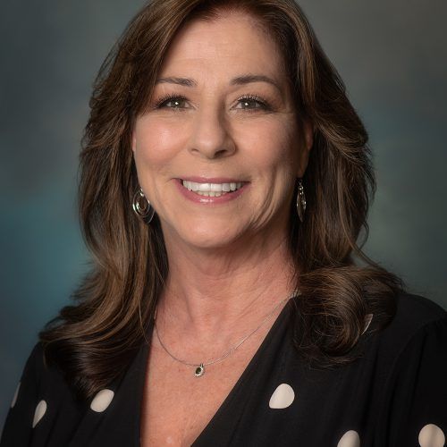 A woman wearing a black polka dot shirt and a necklace is smiling for the camera.