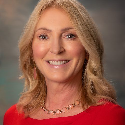 A woman wearing a red shirt and a necklace is smiling for the camera.