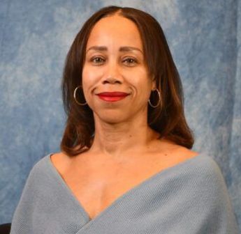 A woman wearing a blue sweater and red lipstick is sitting in front of a blue curtain.