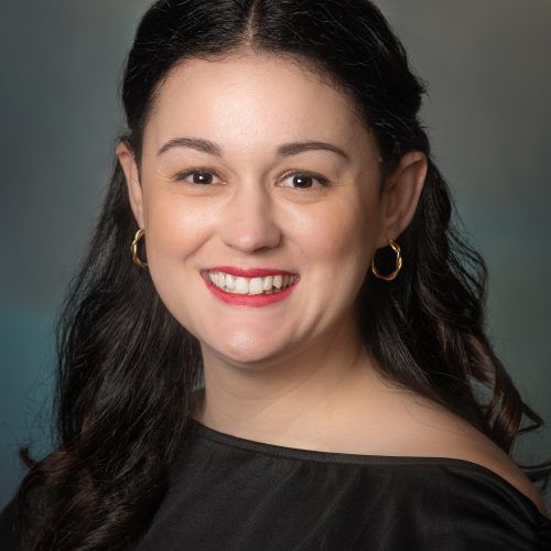 A woman wearing a black shirt and earrings is smiling for the camera.