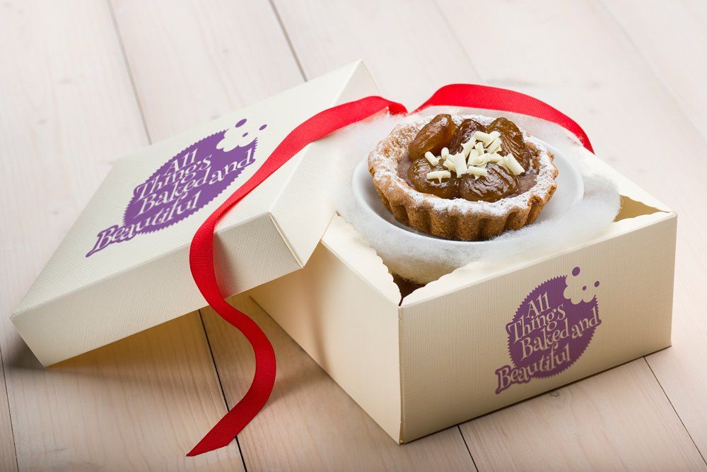 Tart in box tied with red ribbon. White box with logo and tart on a white plate.