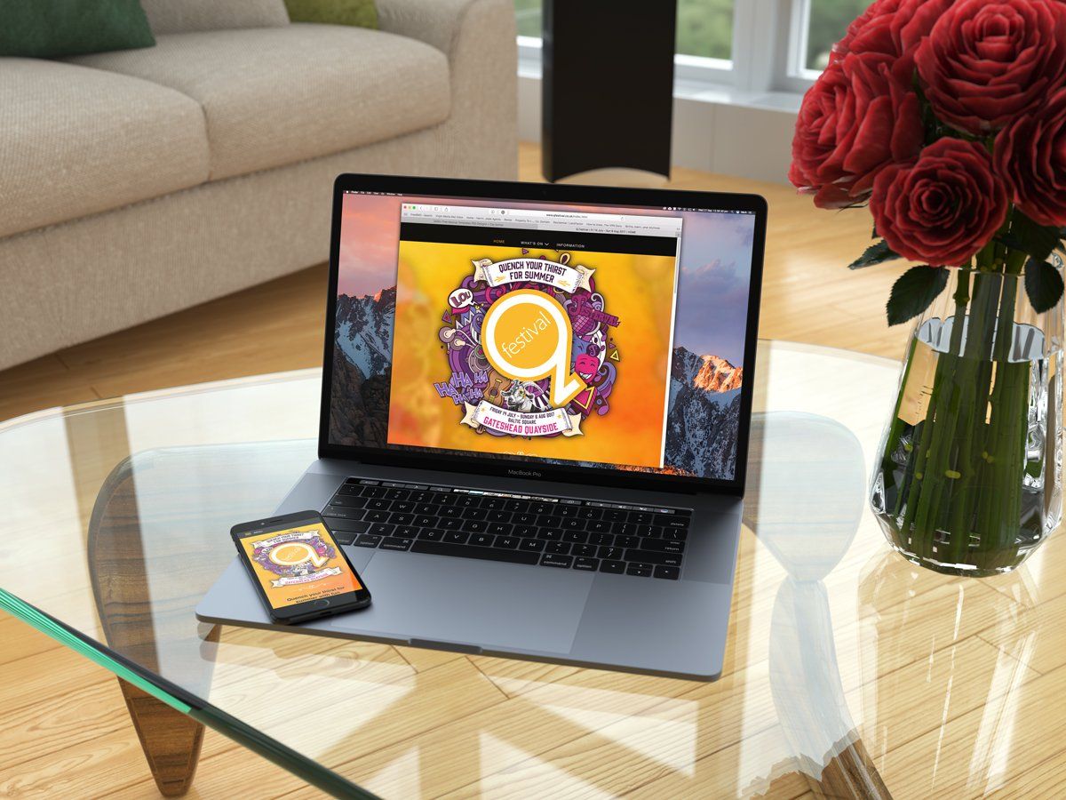 Laptop and phone on glass table displaying a colorful logo, with a bouquet of red roses nearby.
