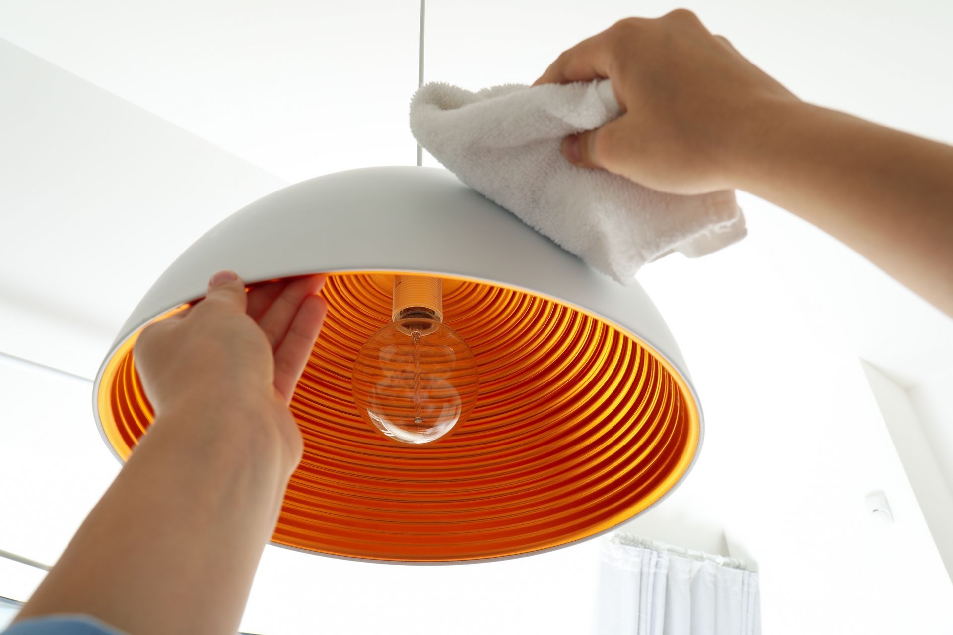 A person is cleaning a light fixture with a towel.