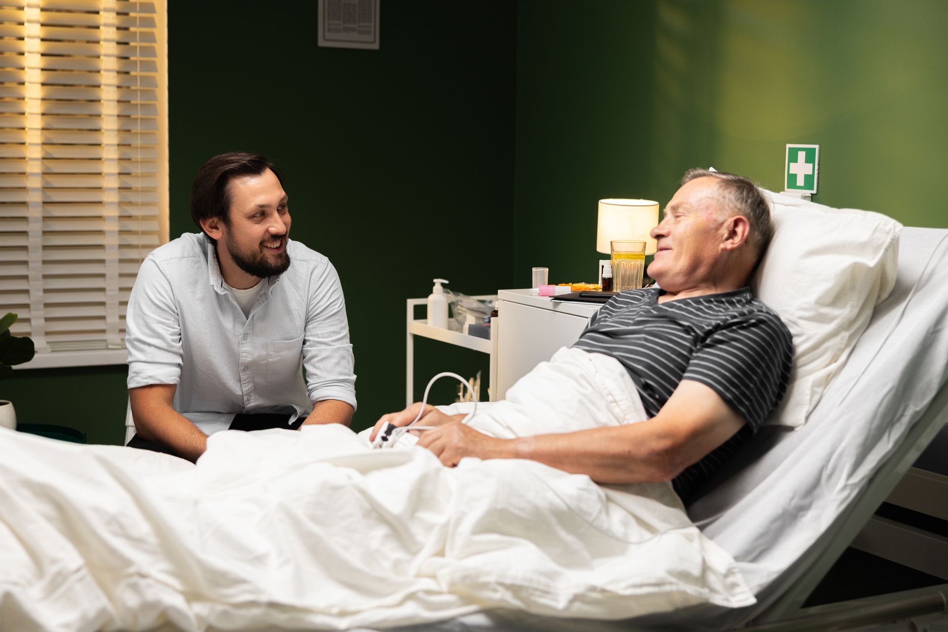 A man is talking to an elderly man in a hospital bed.