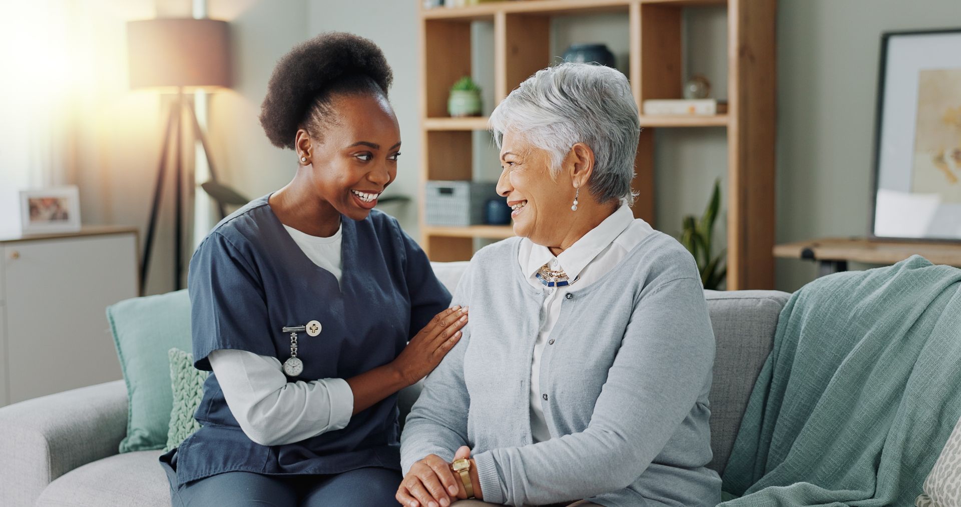 A nurse is sitting on a couch talking to an elderly woman.