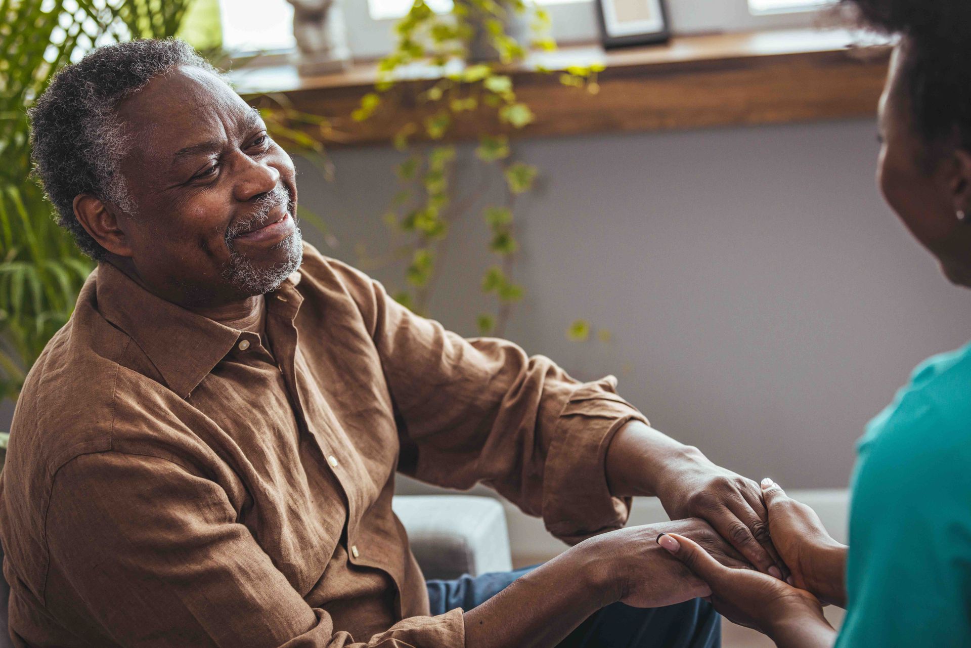 An elderly man is sitting on a couch holding a woman 's hand.