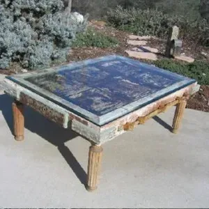 A wooden table with a glass top is sitting on a concrete surface.