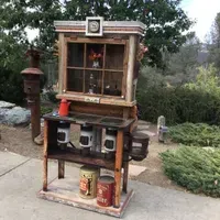 A wooden cabinet with a clock on top of it is sitting on a sidewalk.