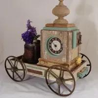 A clock on wheels is sitting on a table next to a vase of flowers.
