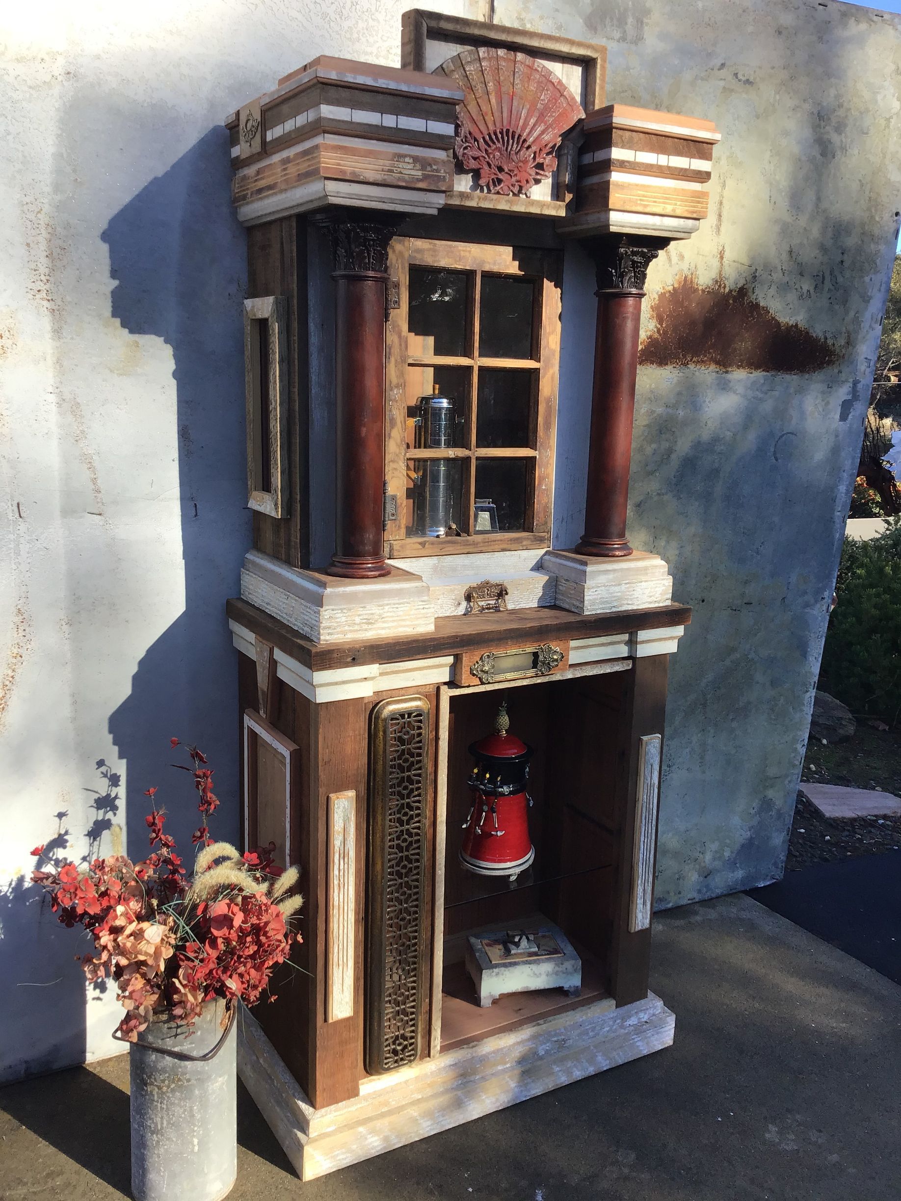 A wooden cabinet with a lantern inside of it is sitting next to a vase of flowers.