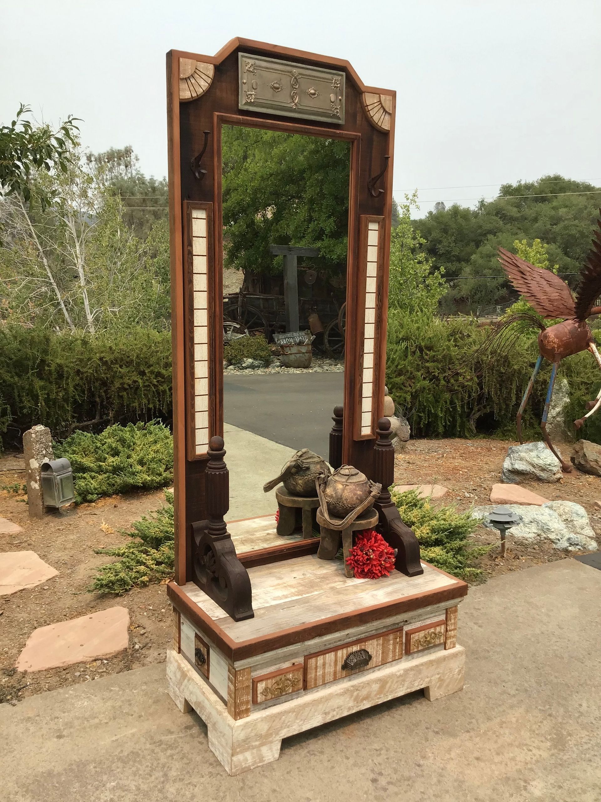 A large mirror is sitting on top of a wooden table in a garden.