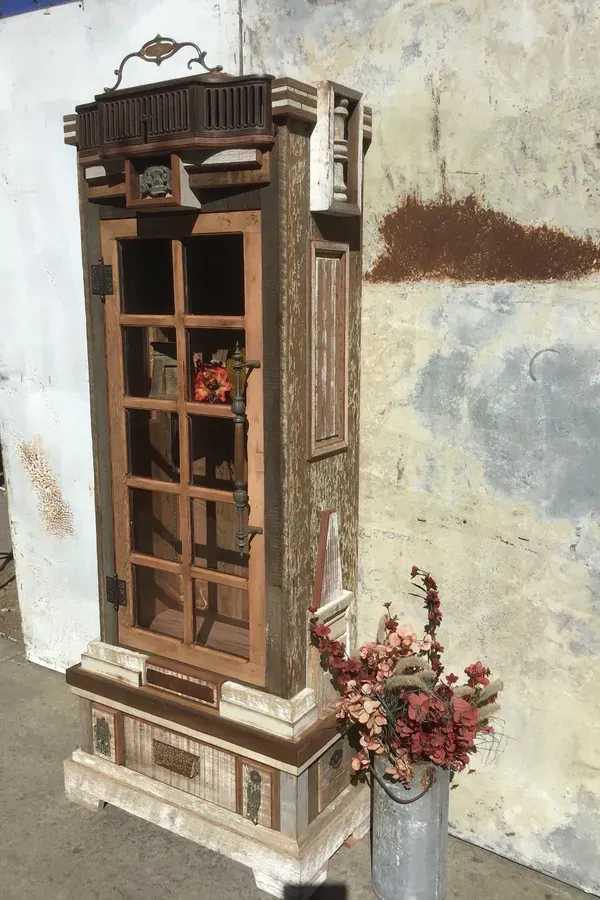 A wooden phone booth is sitting next to a vase of flowers.