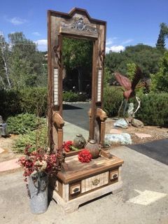 A large mirror is sitting on top of a wooden table in a garden.