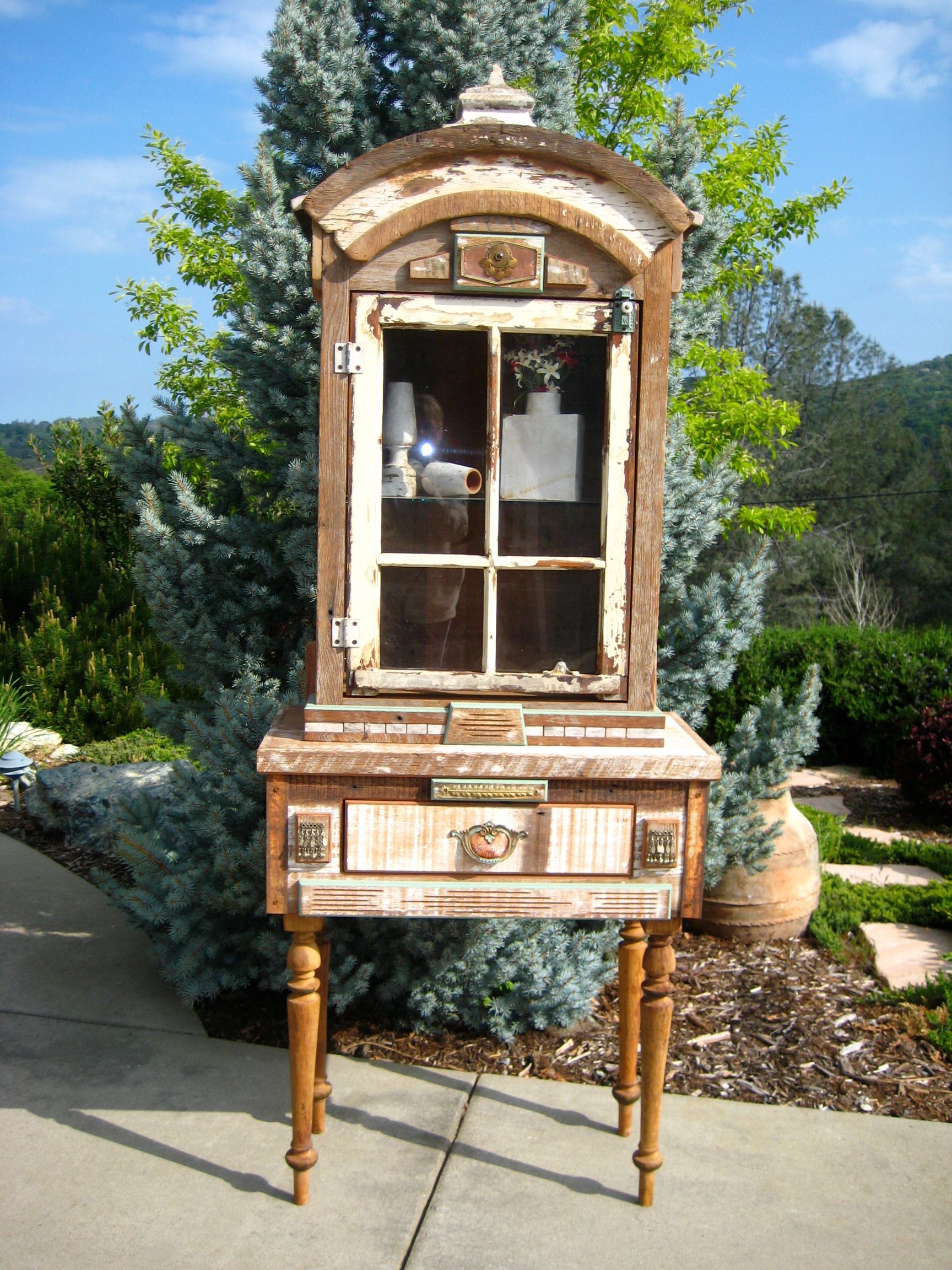A wooden cabinet with a drawer and a window is sitting on top of a wooden table.