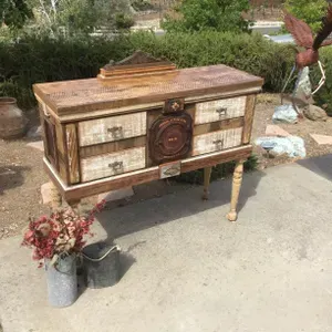A wooden dresser with drawers is sitting on a sidewalk next to a vase of flowers.