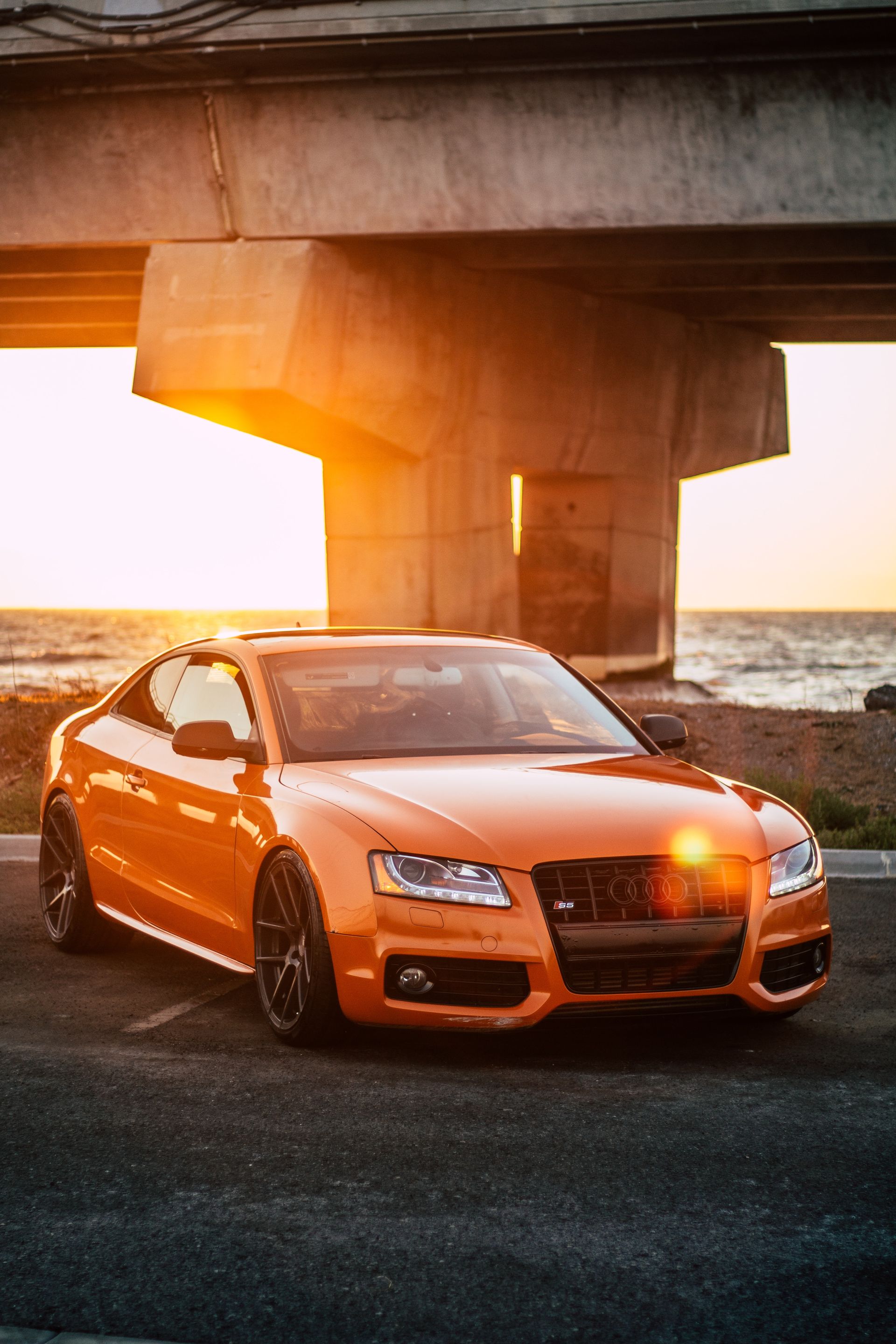 Orange Audi coupe parked under bridge, sunset lighting.