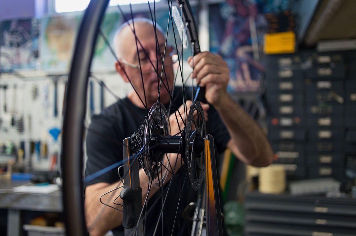 A man is working on a bicycle wheel in a workshop.