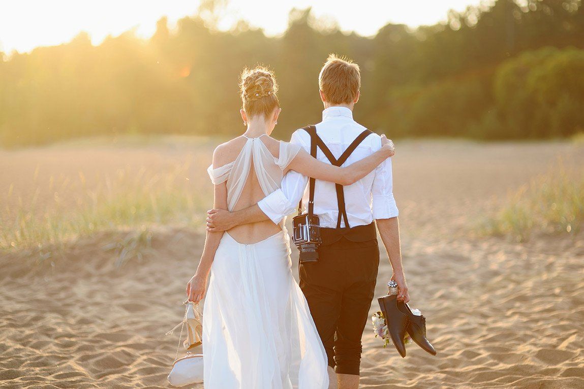 A bride and groom are walking across a sandy field.