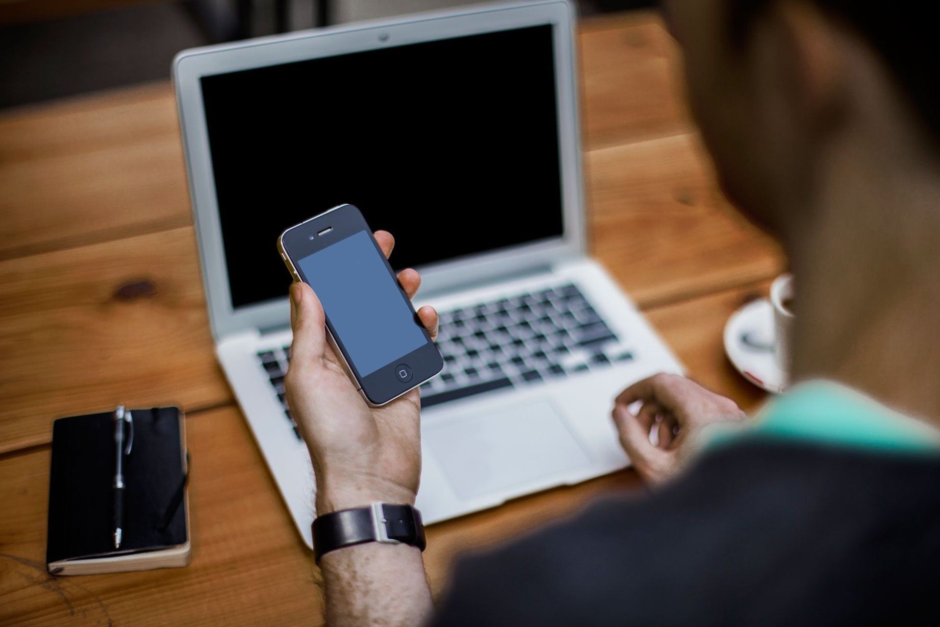 A man is holding a cell phone in front of a laptop computer.