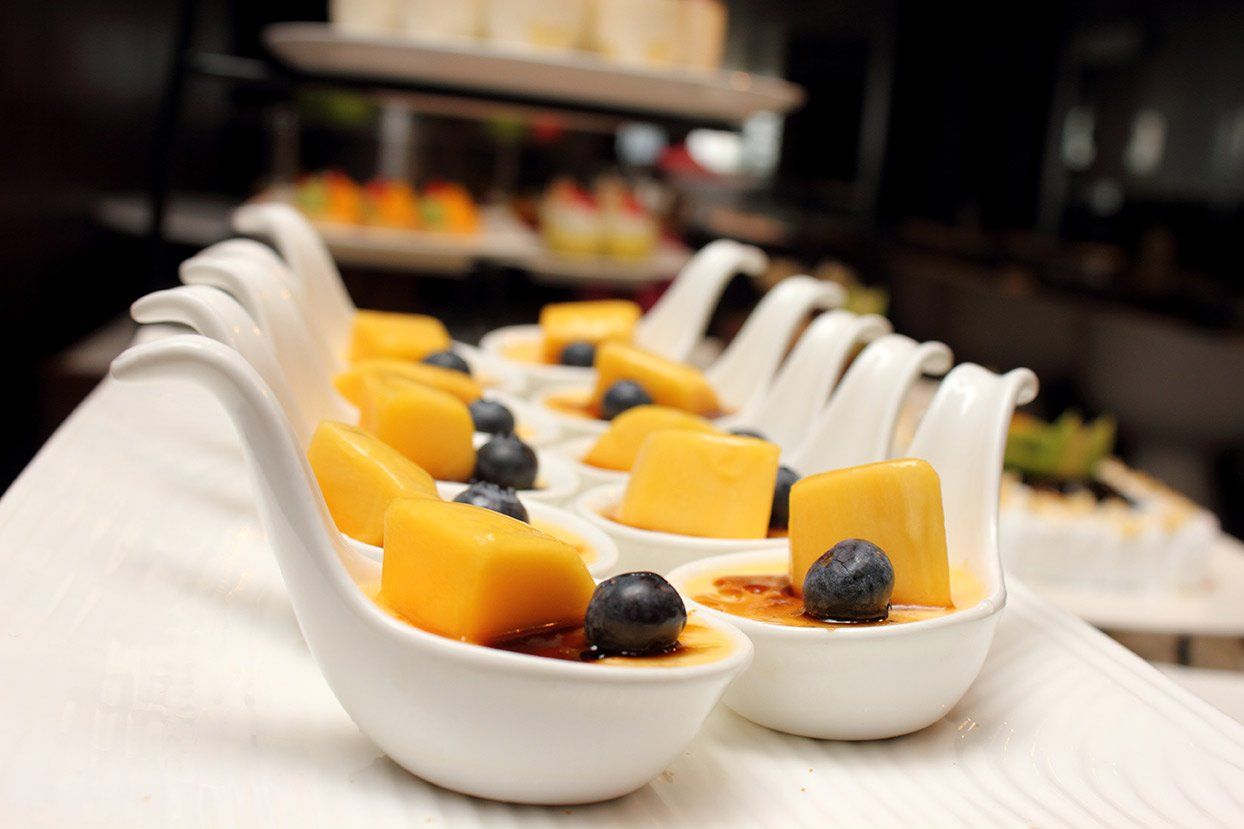 A row of colorful bowls with handles, each filled with fresh fruits such as strawberries, oranges, a