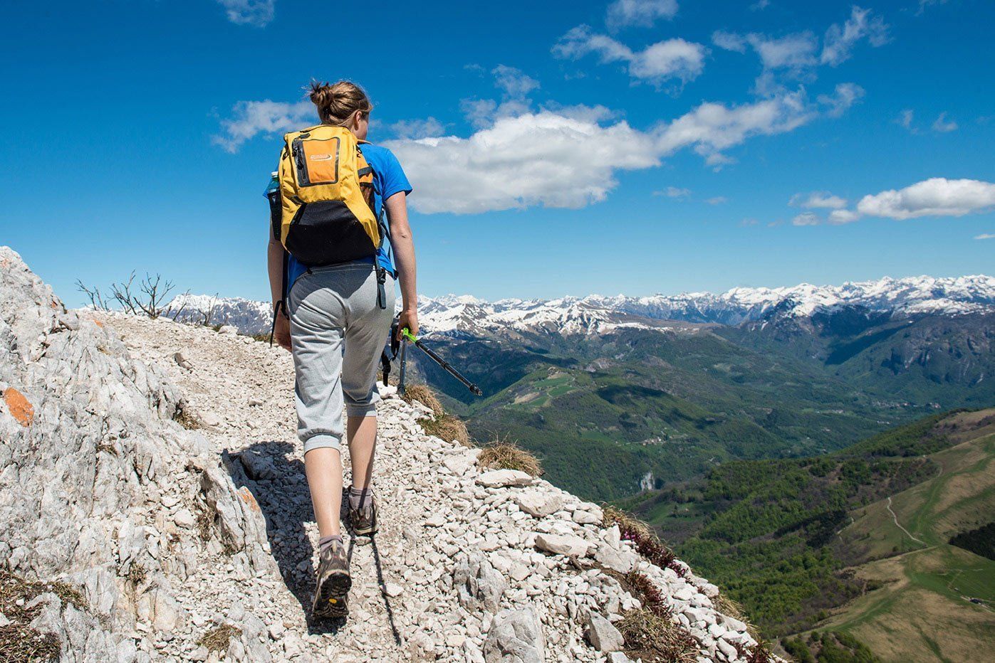 A solo woman hiker, hiking alongside the trail of a mountain, wearing a yellow backpack.