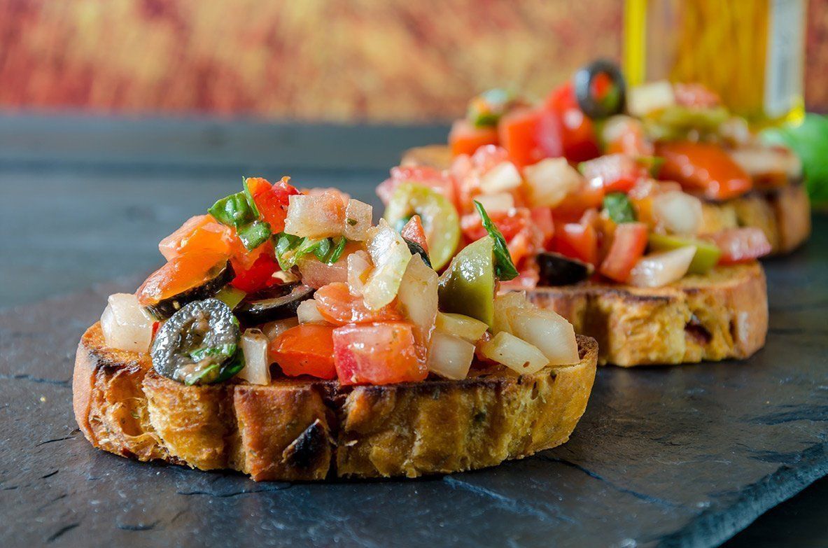 a close up of a sandwich with tomatoes , olives and onions on a table .